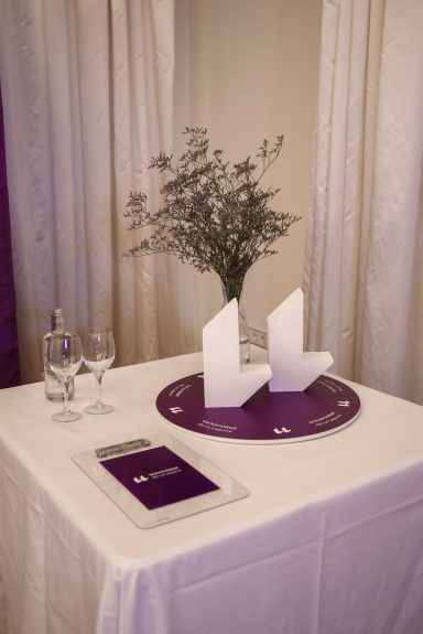 Evento corporativo Mesa con un arreglo floral, dos copas y un cartel en un ambiente decorativo.