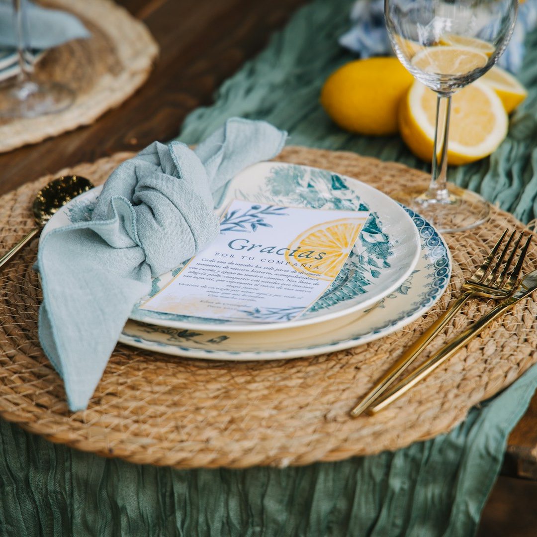 Organización de evento de celebración Mesa decorada con platos, cubiertos dorados, servilleta verde y limones.