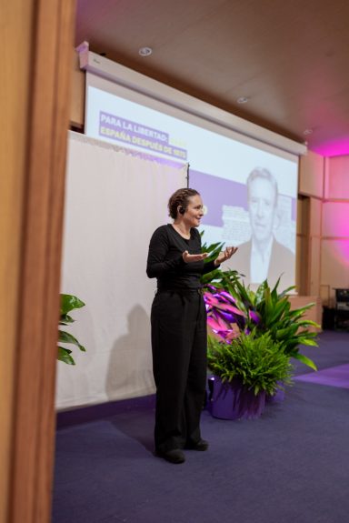 Eventos corporativos Una mujer intérprete de lengua de signos española en un evento, con una presentación proyectada detrás de ella.