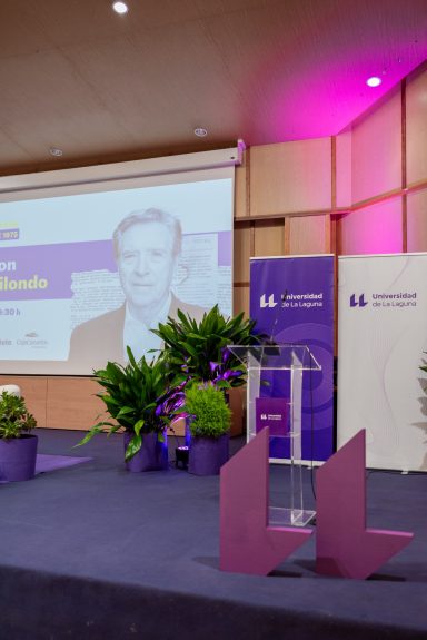 Eventos corporativos Escenario con atril y pantalla, decorado con plantas y luces moradas.