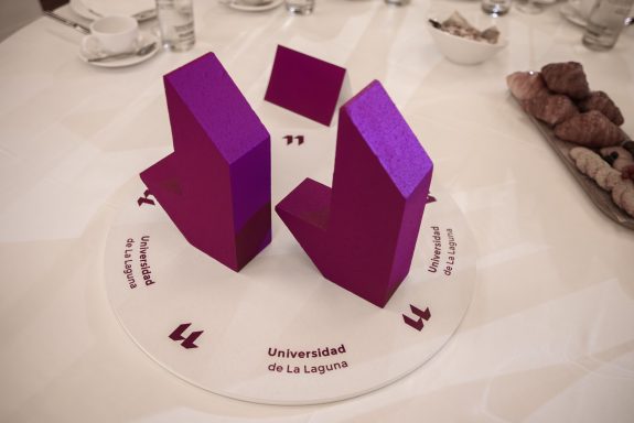 Evento corporativo Tres figuras de color púrpura dispuestas sobre un plato con texto en la base.