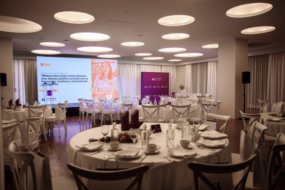 Evento corporativo Salón de eventos con mesas decoradas y pantallas al fondo.