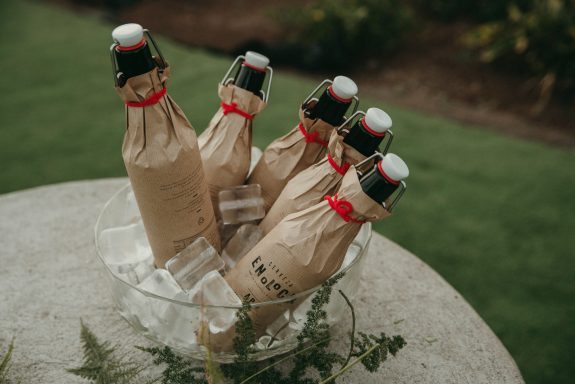 Decoración y catering de eventos Botellas envueltas en papel kraft con cintas rojas, reposando en un recipiente con hielo.