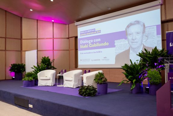 Eventos corporativos Escenario con sillas blancas, plantas decorativas y una pantalla de presentación en un evento.