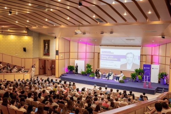 Eventos corporativos Auditorio lleno de personas, con un panel de discusión en un escenario iluminado.